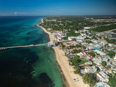 Aerial drone view of white sand beach, blue ocean, resorts, hotels, and a tourist town surrounded by lush green trees. Sunny day, blue sky.  Playa del Carmen, Riviera Maya, Mexico.