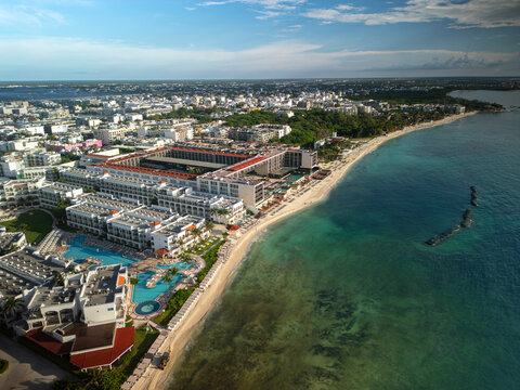 Aerial drone view of white sand beach, blue ocean, resorts, hotels, and a tourist town surrounded by lush green trees. Sunny day, blue sky.  Playa del Carmen, Riviera Maya, Mexico.