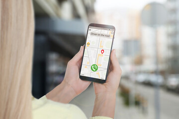 Woman using app on mobile phone to call taxi on city street, closeup