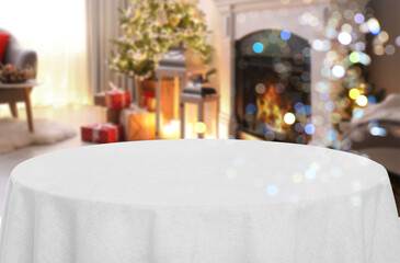 Empty table with white tablecloth in room decorated for Christmas, bokeh lights. Space for design