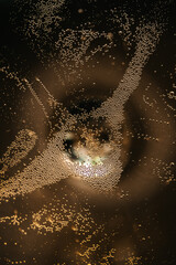 Close-up abstract macro of golden champagne bubbles in glass. Sparkling drink texture with light reflections and circular motion pattern.