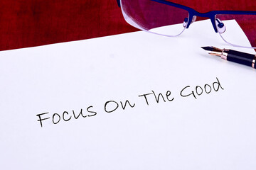 A handwritten message emphasizes the importance of staying positive and focusing on the good in life. Glasses and a pen lie beside it, ready for inspiration