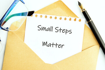 A note with the words small steps matter sits inside a golden envelope next to a fountain pen and a pair of glasses, showcasing motivation and encouragement for daily progress