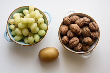 Un cuenco lleno de uvas verdes y otro de nueces, entre ellos un kiwi oro.