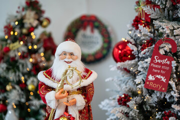 Close-up of a cheerful Santa Claus figurine holding a gift, surrounded by beautifully decorated Christmas trees, a Christmas -themed background for holiday greetings, festive designs