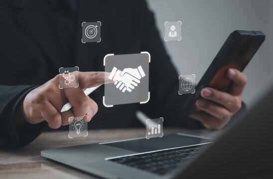 Entrepreneur using stylus to touch digital handshake icon on laptop, representing business partnership, collaboration, teamwork, trust, innovation, and success in modern corporate connection.