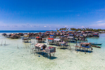 Aerial view of sea gypsy village over clear turquoise waters in Omadal Island Semporna, Sabah, Malaysia. Scenic seascape with coral reefs, coastal village, and blue tropical sky.