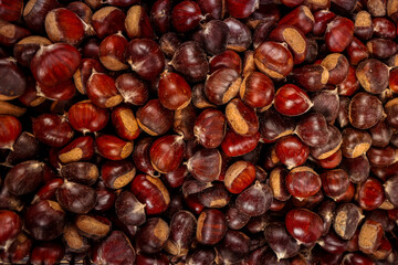 Close-up of fresh chestnuts with shiny brown shells, stacked together in a market display. Autumn harvest concept with natural texture and warm seasonal colors.