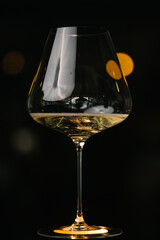 Close-up of wine glass with golden sparkling drink on dark background. Elegant minimalistic composition with reflections and bokeh light.
