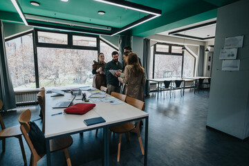 Colleagues gather around a table in a contemporary office to collaborate on a project. The scene showcases natural light and teamwork in a modern workspace equipped with necessary tools and technology
