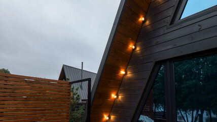 Obraz premium Modern A-frame cabin exterior with string lights and wooden fence