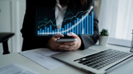 A business professional uses a smartphone to analyze financial data while surrounded by charts and graphs in a modern office, illustrating digital growth. Impute