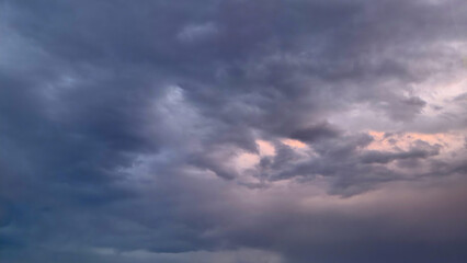 A dark, moody evening sky dominated by heavy, thick stratocumulus clouds in shades of deep gray and indigo, with a subtle hint of pale pink and orange twilight breaking through at the center