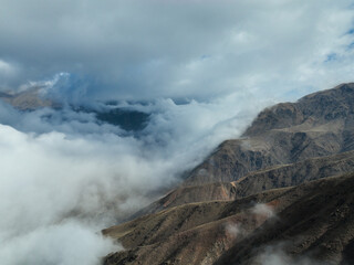 Close aerial view of a dark, steep mountain slope partially shrouded in a thick layer of white clouds under a moody, overcast sky