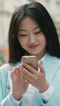 asian businesswoman smiling scrolling smartphone city street slow motion vertical video modern communication digital lifestyle confidence professional woman technology connection urban