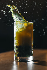 Splash of cocktail in tall glass on dark background. Freeze motion shot with flying droplets and dramatic light. Refreshing drink photography concept.