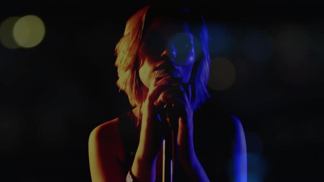 Teenage singer bringing microphone to lips and starting music performance under colored spotlights