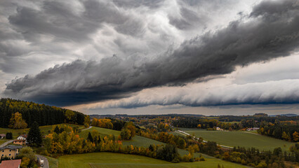 Massive storm front with rolling arcus cloud and heavy rainfall passing through Bavarian landscape under moody autumn sky