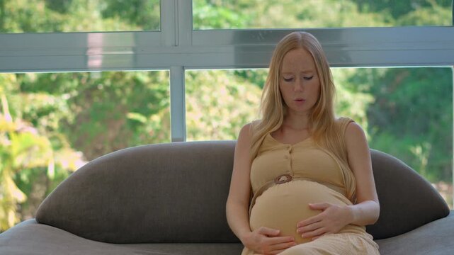 Pregnant woman practicing deep breathing exercises to release tension during early labor contractions, preparing mentally and physically for the childbirth process at home. Slowmotion video.