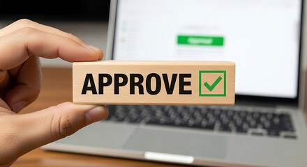 Hand holding wooden block with approve text and checkmark in front of laptop approval agreement