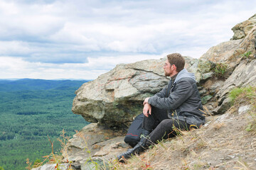 A man in a gray jacket is sitting on a mountain top.