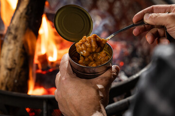 Hands holding a can of baked beans by the fire