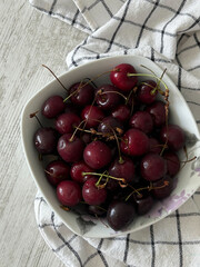 White bowl with fresh dark red cherries on a checkered cloth. Used in food, nutrition, and healthy eating materials.