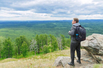 A man in a gray jacket stands on a mountain peak in full growth.