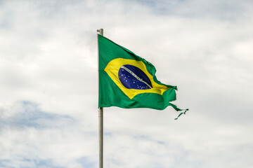 Bandeira brasileira rasgada e desgastada tremulando ao vento em um dia nublado.