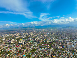 Expansive high aerial panorama of the sprawling city of Bishkek, stretching out below the distant, snow-capped Tien Shan mountain range