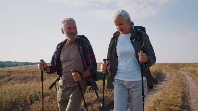 Happy mature partners with rucksacks hike at autumn farmland