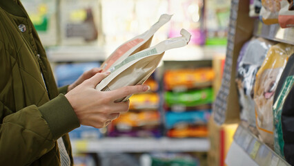 A woman comparing two packages of dry pet food in a store, holding them in her hands and deciding which one to buy. Consumer choice, healthy nutrition and responsible pet owner in retail environment.