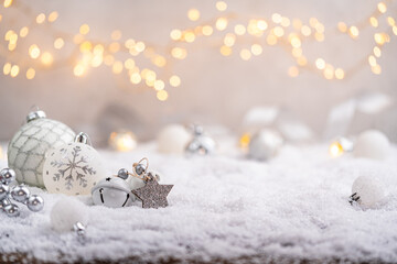 Elegant silver and white ornaments, stars, and bells lie on snow with glowing lights in the...
