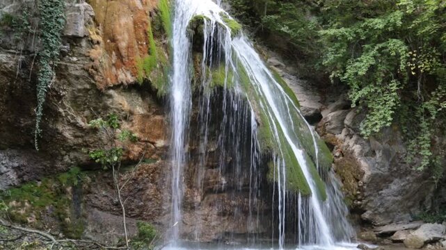 Jum Jum waterfall in the forest on a green background on a bright sunny day. Flora nature plants sights of Russia.
