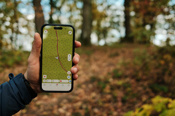 Close-up of man holding smartphone with GPS navigation app while hiking in autumn forest of Fruska...