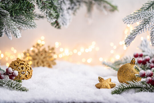 Glittering gold ornaments and snowflakes rest on snowy ground with frosted pine branches and soft glowing lights. Winter Christmas Holiday Decoration Background