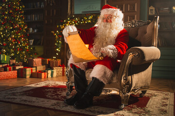 Merry Christmas. Happy Santa Claus reading wish list paper roll in festive living room with...