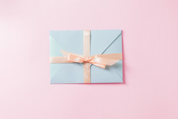 Light blue envelope with a pink ribbon on a pastel pink background