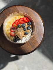 Yogurt granola fruit bowl with peanut butter and berries on wooden stool, top view, sunlight