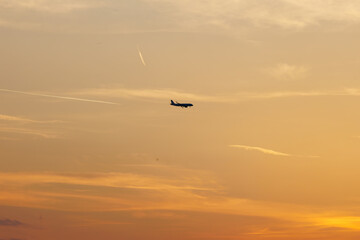 Airplane silhouette against a golden sunset sky with contrails