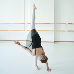Obraz premium Female ballet dancer performing impressive stretch in bright dance studio.