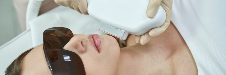 Young caucasian female undergoing facial laser hair removal treatment at a dermatology clinic.