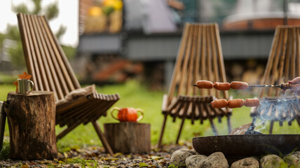 Cozy outdoor grilling scene with sausages cooking over a fire pit on a beautiful day