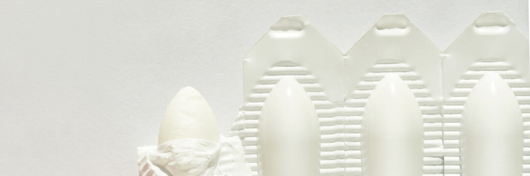 Close-up of white suppositories in packaging against light background.