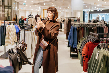 Senior woman comparing clothes using smartphone in boutique