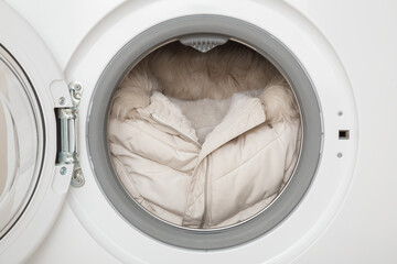 White warm female winter jacket with fur hood in opened washing machine. Clothes care. Closeup....