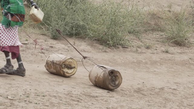 Beautiful African woman pushes two heavy water canisters attached to a rope. 