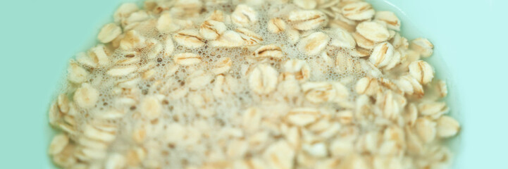 Close-up of soaking rolled oats in water on a light green background for healthy breakfast preparation.