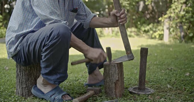 A man diligently sharpens a traditional farming tool outdoors, using a hammer and wooden block. This authentic scene of manual labor captures the rustic process with clear natural sounds.