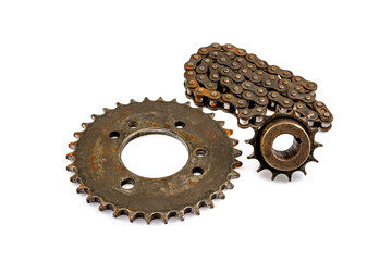 A close-up of a dirty, oily, and greasy chain, sprockets, and wheel hub on an old motorcycle against a white background. The image captures the essence of repair and maintenance.